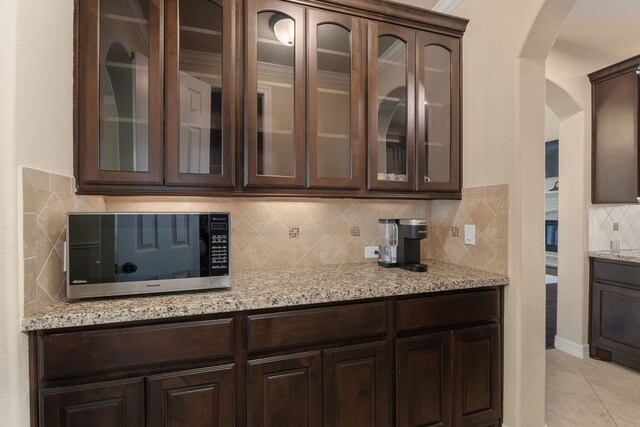 11702 Saporito Way, Richmond, TX 77406 - kitchen with stainless steel microwave, arched walkways, dark brown cabinetry, decorative backsplash, and light stone counters