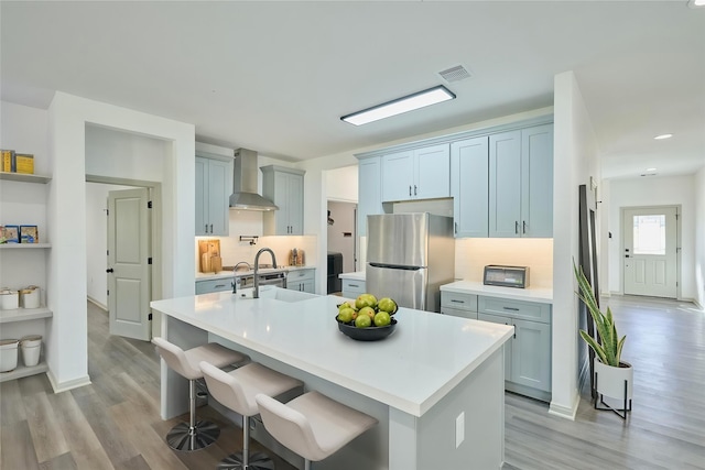 4 Hanover Ln, Panorama Village, TX 77304 - kitchen featuring wall chimney range hood, freestanding refrigerator, light wood-style floors, tasteful backsplash, and light countertops