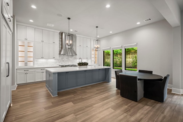 19 Pronghorn Pl, The Woodlands, TX 77389 - kitchen featuring wall chimney range hood, white cabinetry, wood finished floors, gray cabinetry, and decorative backsplash