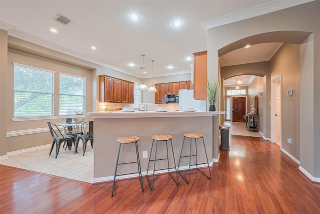 2500 Amy Lee Dr, Conroe, TX 77304 - kitchen with black microwave, arched walkways, freestanding refrigerator, a breakfast bar, and light wood-style flooring