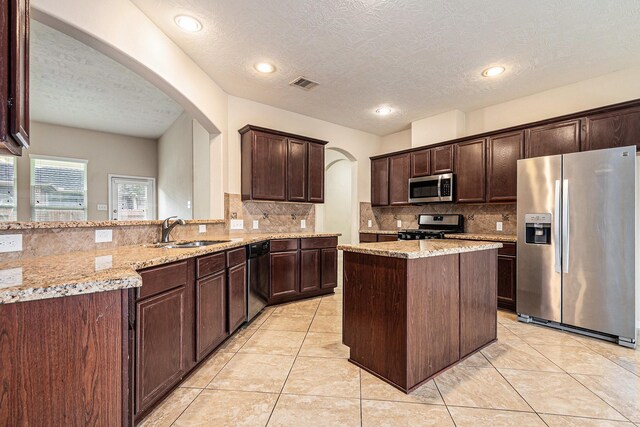 30710 Basil Trace Dr, Spring, TX 77386 - kitchen with stainless steel appliances, a sink, a textured ceiling, arched walkways, and dark brown cabinetry