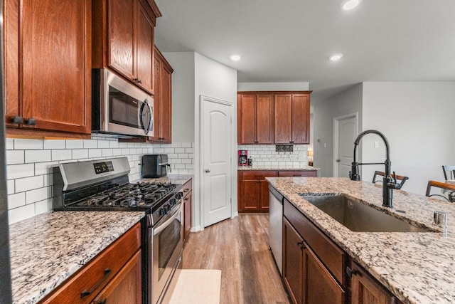 819 Spruce Pine Dr, Conroe, TX 77318 - kitchen with appliances with stainless steel finishes, a sink, light wood-style floors, light stone counters, and backsplash