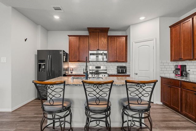 819 Spruce Pine Dr, Conroe, TX 77318 - kitchen featuring stainless steel appliances, an island with sink, tasteful backsplash, light stone counters, and dark wood finished floors