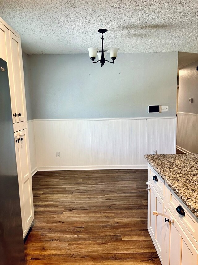 1301 Cherie Brook Dr, Goliad, TX 77963 - unfurnished dining area with wainscoting, a textured ceiling, dark wood-type flooring, and a chandelier