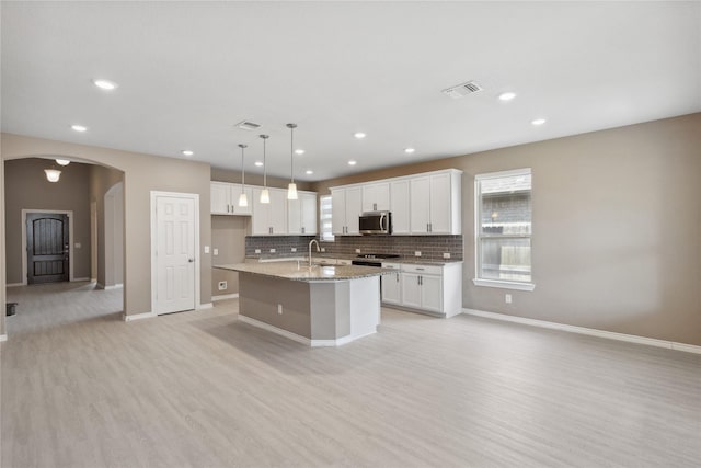 24730 Harbor Terrace Ln, Richmond, TX 77406 - kitchen featuring stainless steel microwave, arched walkways, light wood-type flooring, white cabinetry, and a kitchen island with sink