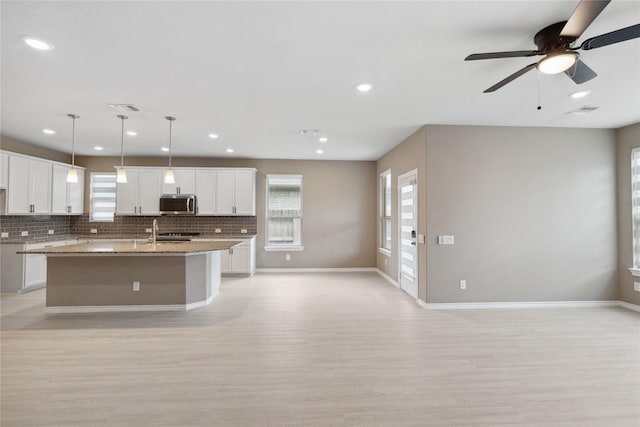 24730 Harbor Terrace Ln, Richmond, TX 77406 - kitchen featuring stainless steel microwave, light wood-style floors, tasteful backsplash, a kitchen island with sink, and open floor plan