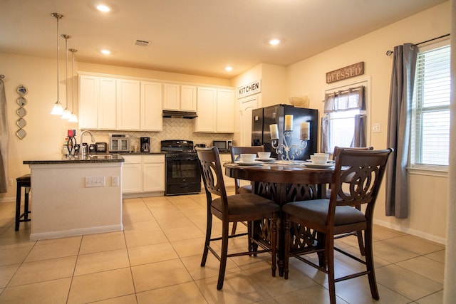 7735 Nevaeh Crest Path, Houston, TX 77016 - kitchen with black appliances, decorative backsplash, under cabinet range hood, white cabinetry, and light tile patterned floors
