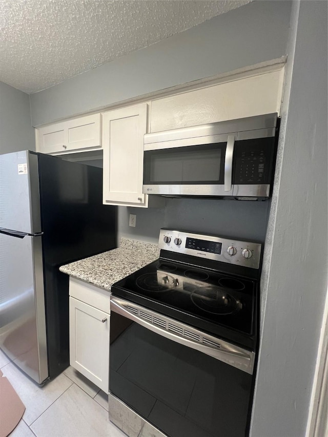 3724 Woodchase Dr Unit 3724, Houston, TX 77042 - kitchen with stainless steel appliances, a textured ceiling, white cabinets, light tile patterned floors, and light stone countertops