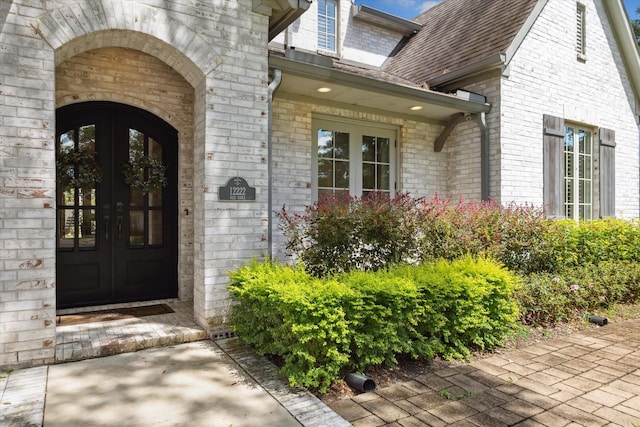 entrance to property with french doors, brick siding, stone siding, and roof with shingles