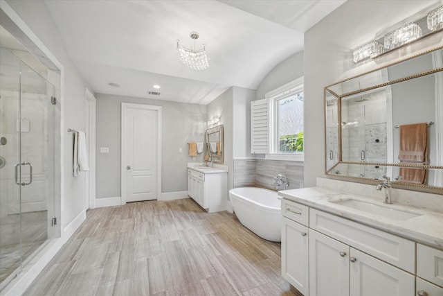 bathroom featuring a stall shower, a freestanding bath, two vanities, a chandelier, and wood finished floors