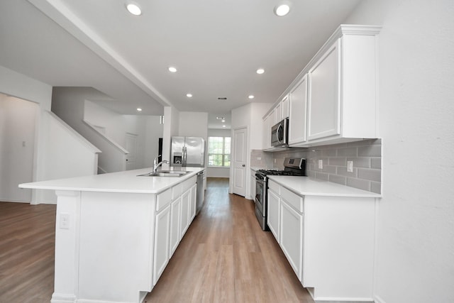 24063 Hawthorn Lakes Dr, New Caney, TX 77357 - kitchen with appliances with stainless steel finishes, light wood-style flooring, a sink, white cabinets, and light countertops