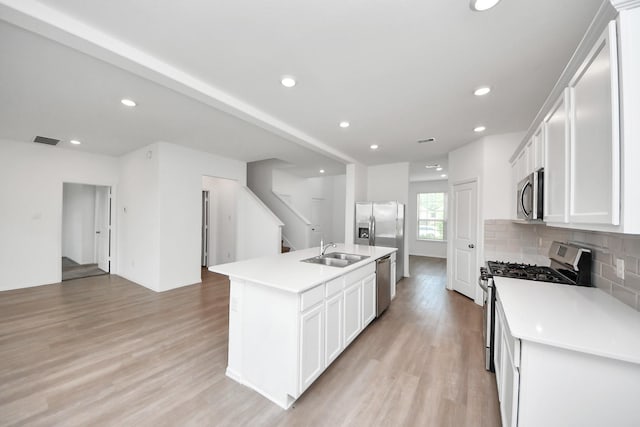 24063 Hawthorn Lakes Dr, New Caney, TX 77357 - kitchen featuring stainless steel appliances, a sink, light wood-style flooring, a center island with sink, and tasteful backsplash
