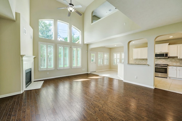 24635 Blue Opal Ln, Katy, TX 77494 - unfurnished living room featuring a ceiling fan, wood finished floors, a tile fireplace, a high ceiling, and baseboards