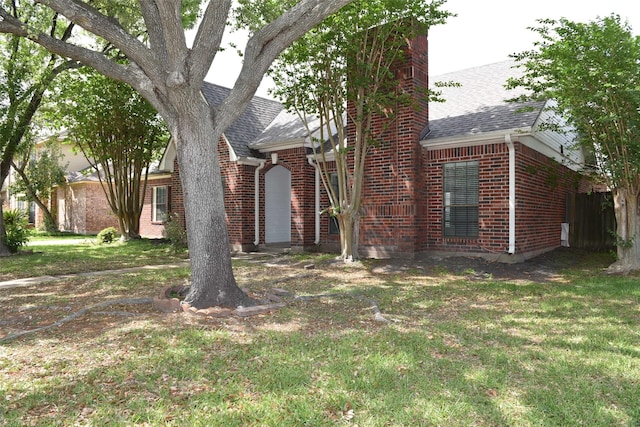 view of front of house featuring brick siding, a shingled roof, a chimney, and a front lawn