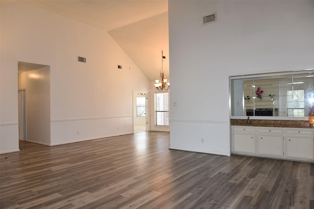 unfurnished living room with high vaulted ceiling, a chandelier, and dark wood-style floors
