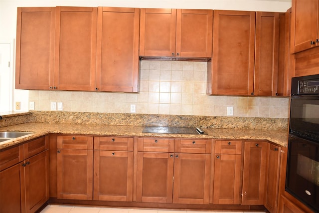 kitchen featuring black appliances, light stone counters, tasteful backsplash, and a sink