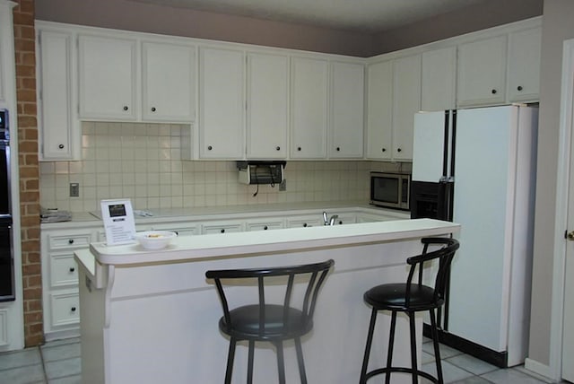 2118 Linea Del Pino St, Houston, TX 77077 - kitchen featuring freestanding refrigerator, stainless steel microwave, tasteful backsplash, white cabinets, and a kitchen breakfast bar