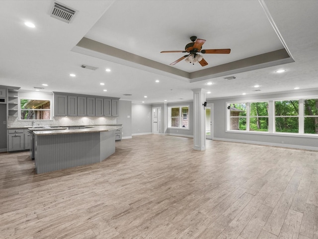 5401 Palm Dr, Dickinson, TX 77539 - unfurnished living room with ceiling fan, a tray ceiling, light wood-type flooring, baseboards, and decorative columns