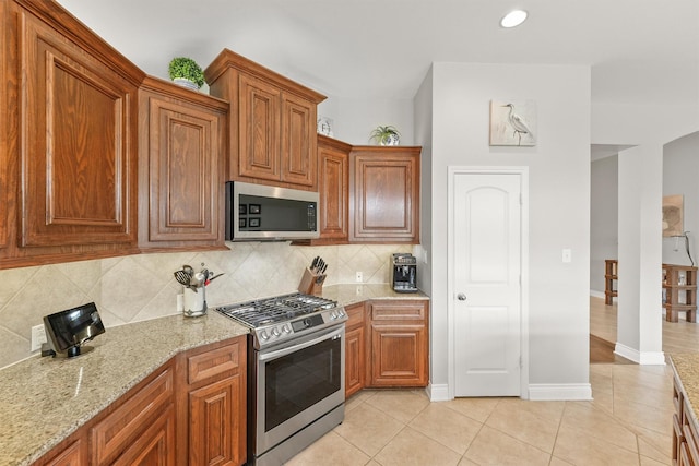 31815 Forest Oak Ln, Conroe, TX 77385 - kitchen featuring appliances with stainless steel finishes, backsplash, light stone countertops, light tile patterned floors, and baseboards