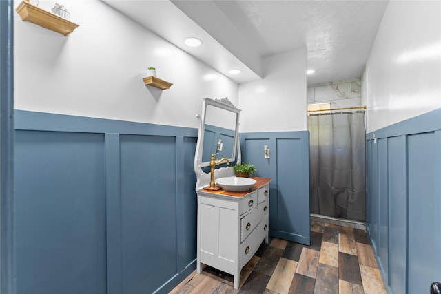 14232 Calhoun Rd, Conroe, TX 77302 - full bathroom with a shower with shower curtain, vanity, a wainscoted wall, wood finished floors, and a decorative wall