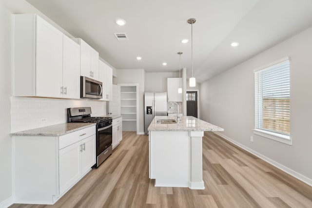 18733 Bliss Pl, New Caney, TX 77357 - kitchen featuring stainless steel appliances, a sink, decorative backsplash, light wood-style flooring, and white cabinets