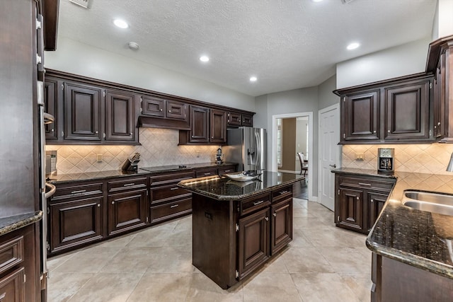 17718 Dove Tree Ln, Spring, TX 77379 - kitchen with stainless steel fridge with ice dispenser, dark stone countertops, tasteful backsplash, dark brown cabinets, and a kitchen island