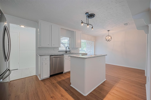 kitchen featuring appliances with stainless steel finishes, a textured ceiling, white cabinets, a sink, and a kitchen island