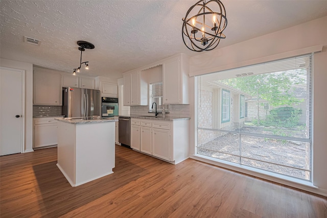 kitchen with appliances with stainless steel finishes, a sink, wood finished floors, backsplash, and a textured ceiling
