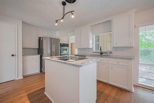 kitchen featuring a sink, stainless steel appliances, a center island, light wood-style floors, and backsplash