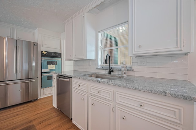 kitchen featuring appliances with stainless steel finishes, a sink, white cabinetry, a textured ceiling, and decorative backsplash