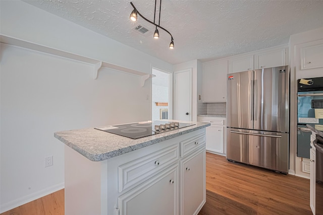 kitchen with stainless steel appliances, wood finished floors, white cabinetry, light countertops, and a textured ceiling