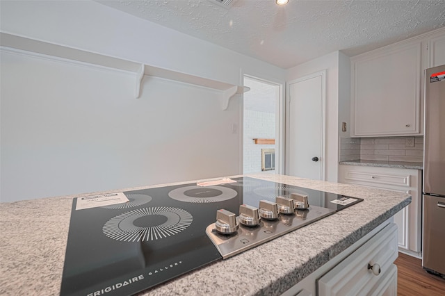 kitchen with black electric cooktop, freestanding refrigerator, a textured ceiling, white cabinetry, and decorative backsplash