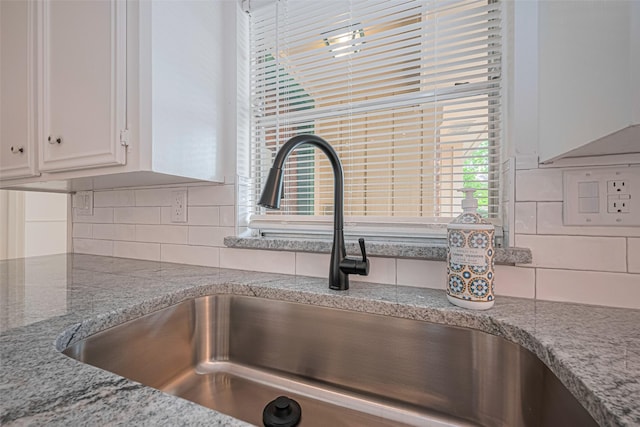 kitchen view of a sink, white cabinetry, decorative backsplash, and light stone countertops