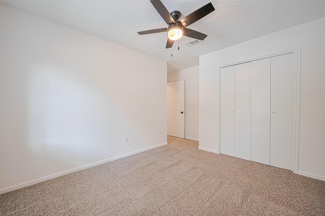 unfurnished bedroom with a textured ceiling, carpet floors, a closet, baseboards, and a ceiling fan