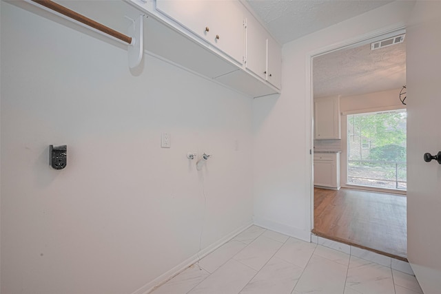 clothes washing area featuring cabinet space, a textured ceiling, light marble finish floors, and baseboards