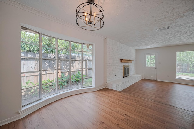 unfurnished living room with a chandelier, baseboards, a textured ceiling, wood finished floors, and a fireplace