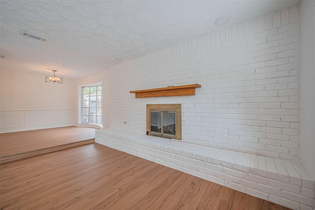 unfurnished living room with a textured ceiling, a fireplace, wood finished floors, and a chandelier