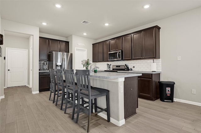 21626 Sage Landing Ln, Katy, TX 77449 - kitchen with appliances with stainless steel finishes, light wood-style floors, a breakfast bar area, backsplash, and a kitchen island with sink
