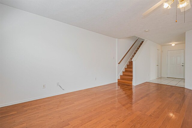 8223 Golf Green Cir, Houston, TX 77036 - unfurnished room with light wood-style flooring, stairway, a ceiling fan, baseboards, and a textured ceiling