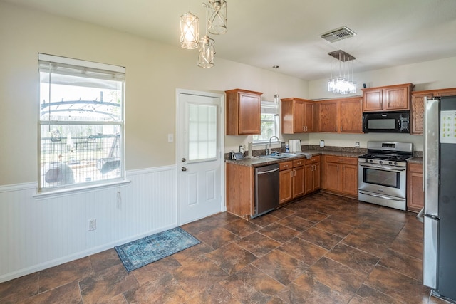3911 Falvel Cove Dr, Spring, TX 77388 - kitchen featuring stainless steel appliances, a sink, a chandelier, a wainscoted wall, and brown cabinets