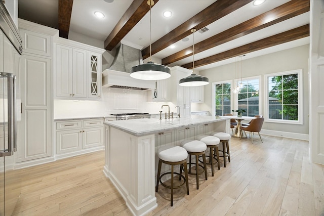 4654 Ingersoll St, Houston, TX 77027 - kitchen featuring beam ceiling, light wood-style floors, a kitchen bar, white cabinets, and glass insert cabinets
