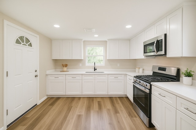 3108 Memel St, Houston, TX 77026 - kitchen featuring stainless steel appliances, a sink, light wood-type flooring, white cabinetry, and light countertops