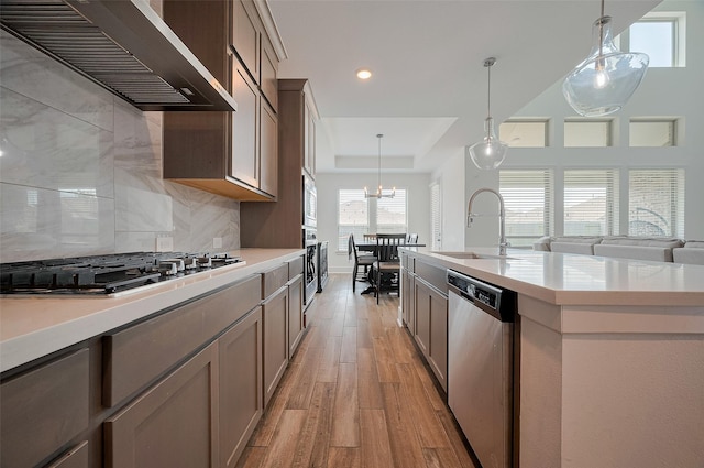 23604 Olive Creek Ln, New Caney, TX 77357 - kitchen with wall chimney exhaust hood, appliances with stainless steel finishes, a sink, light wood finished floors, and a raised ceiling