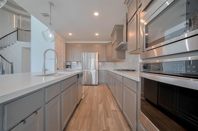 23604 Olive Creek Ln, New Caney, TX 77357 - kitchen featuring appliances with stainless steel finishes, gray cabinetry, a sink, light wood-type flooring, and decorative backsplash