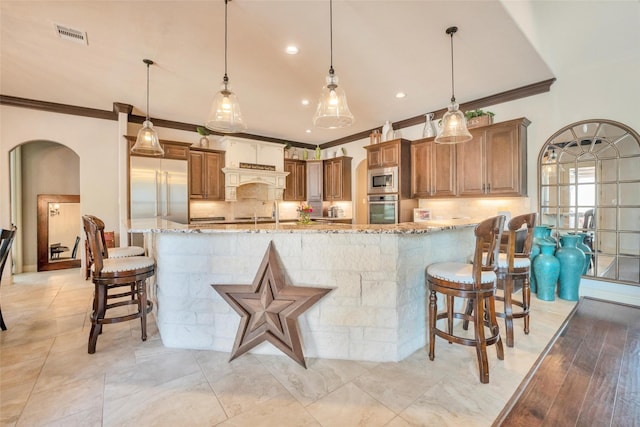40610 Ithaca Ln, Magnolia, TX 77354 - kitchen featuring built in appliances, crown molding, light stone countertops, arched walkways, and a kitchen bar