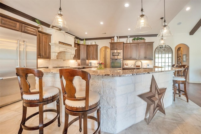 40610 Ithaca Ln, Magnolia, TX 77354 - kitchen with built in appliances, a large island with sink, backsplash, arched walkways, and a breakfast bar