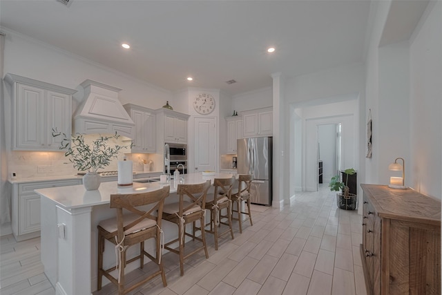 10615 Winding Arbor Ct, Cypress, TX 77433 - kitchen featuring appliances with stainless steel finishes, custom range hood, backsplash, a kitchen island with sink, and ornamental molding
