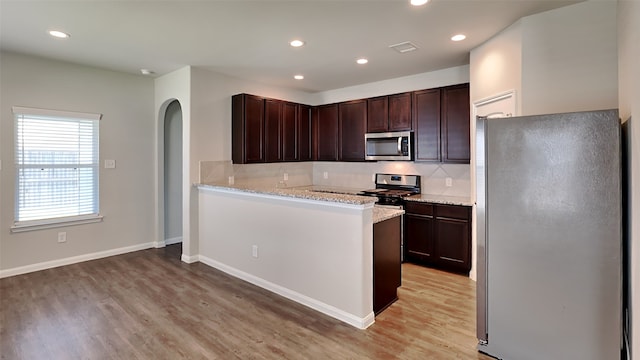 24734 Signorelli Way, Katy, TX 77493 - kitchen featuring stainless steel appliances, light wood-type flooring, backsplash, arched walkways, and dark brown cabinetry