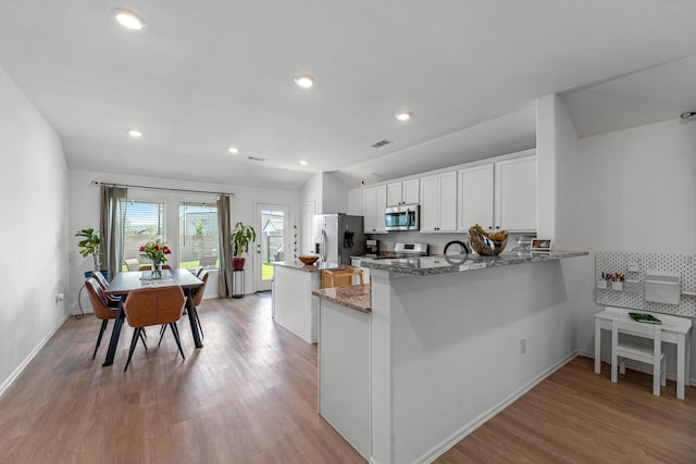 21411 Waldenburg Pl, Tomball, TX 77375 - kitchen featuring stainless steel appliances, light wood-style floors, a center island, light stone countertops, and white cabinets