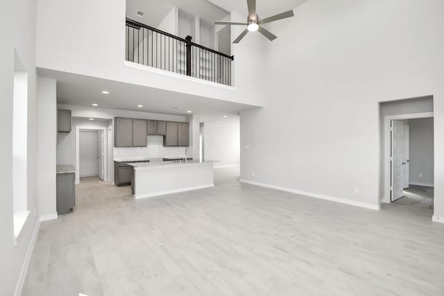 12027 Maple Oak Dr, Houston, TX 77066 - unfurnished living room featuring a high ceiling, baseboards, a ceiling fan, light wood finished floors, and a sink